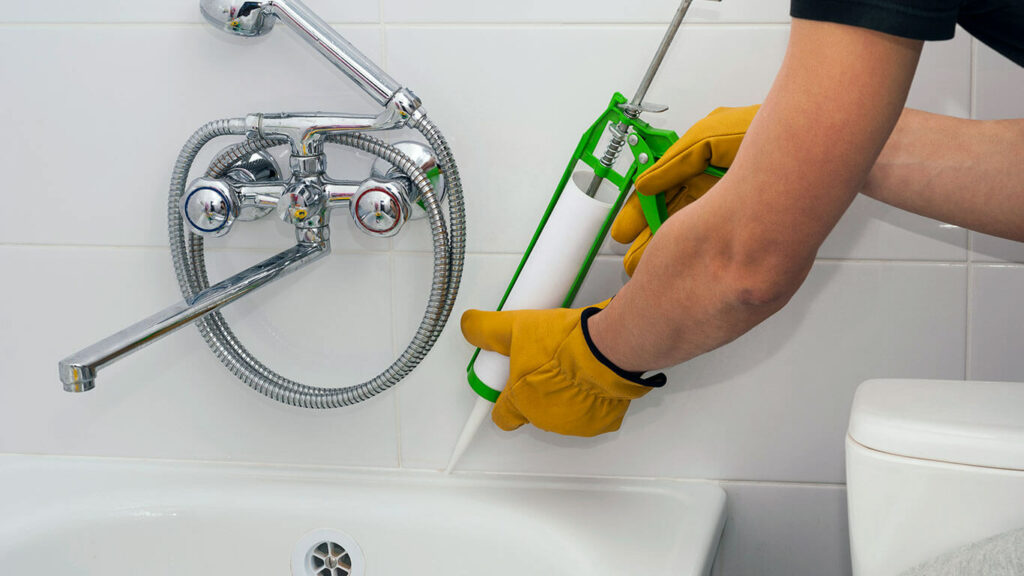 Fontanero arreglando la junta de un baño agregando silicona